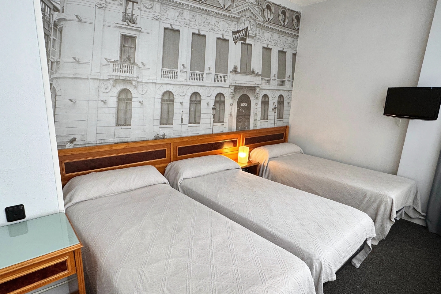 Habitación triple del Hotel Photo Zabalburu con tres camas individuales y mural decorativo de Bilbao